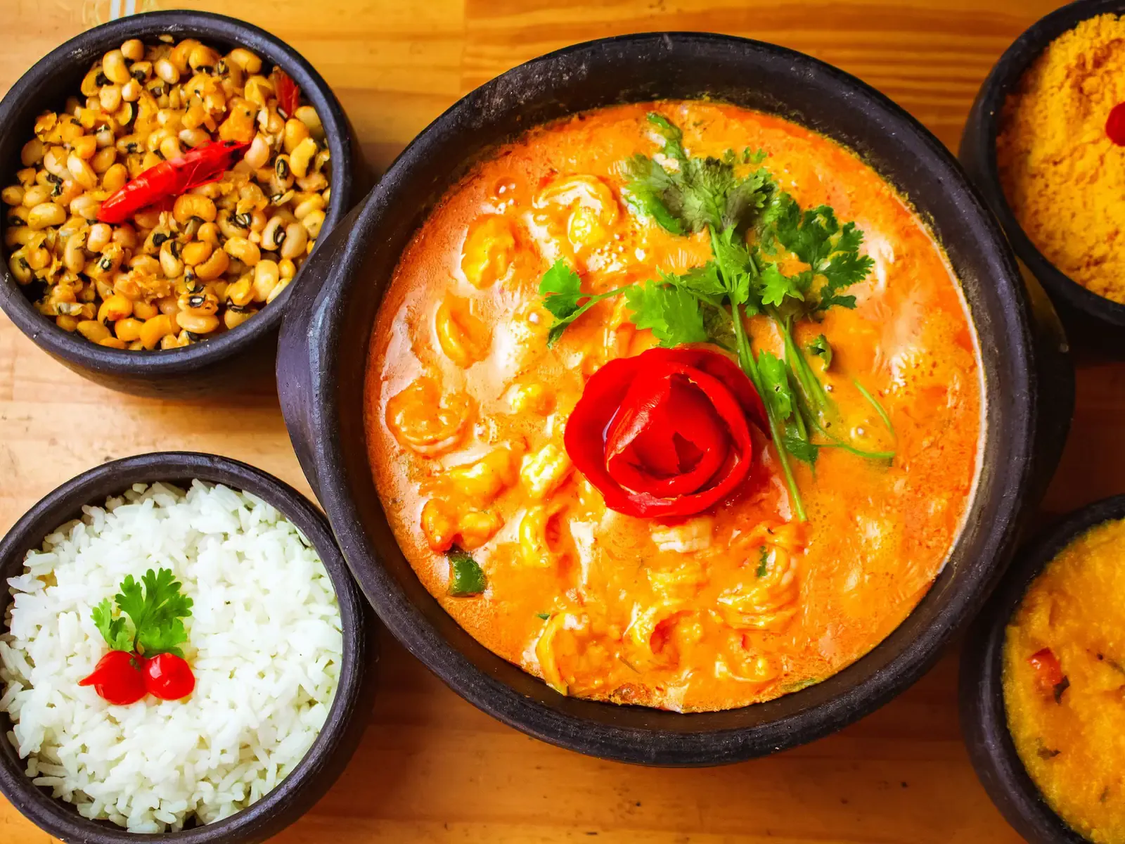 Garnelen-Moqueca in einer dunklen Tonschale, dazu Reis, Farofa, Augenbohnen und Pirão